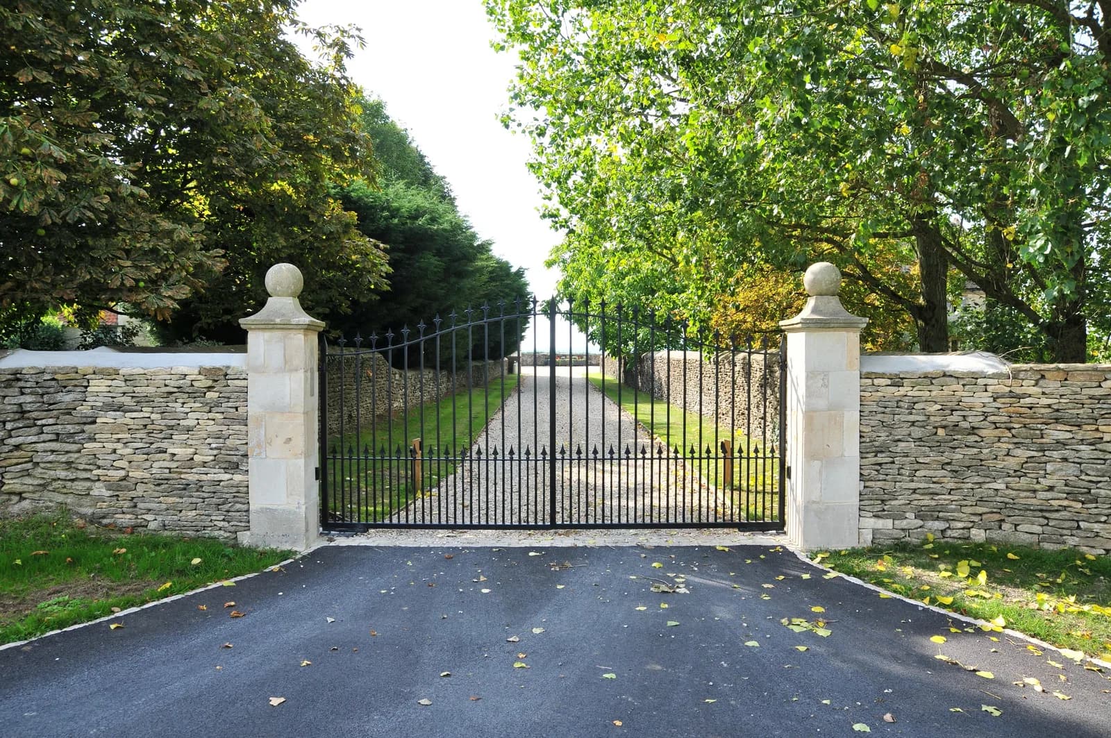 Iron gates between stone piers, with a gravel drive running away between clipped hedges