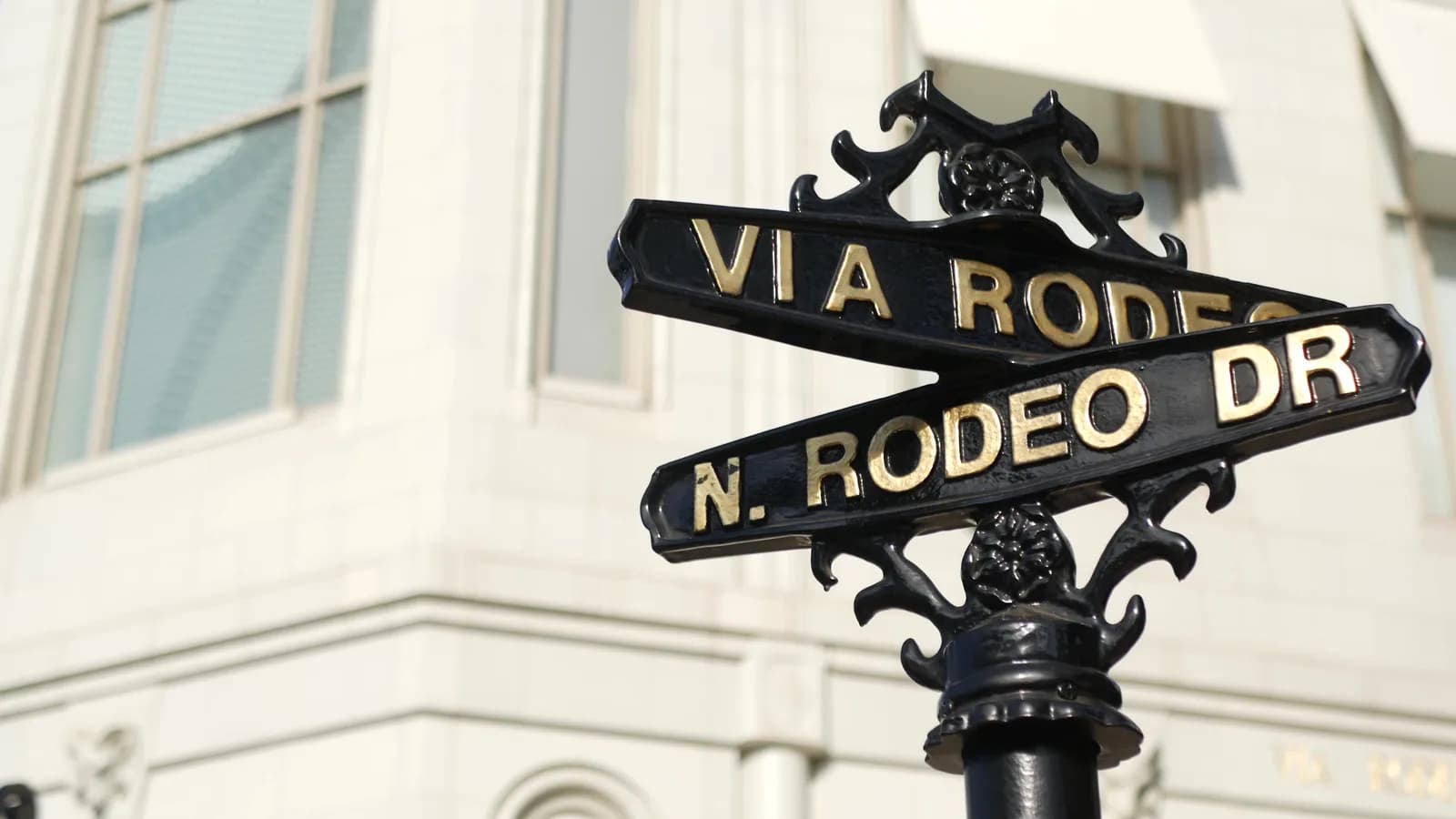 The black and gold Via Rodeo and North Rodeo Drive street sign against a stone facade