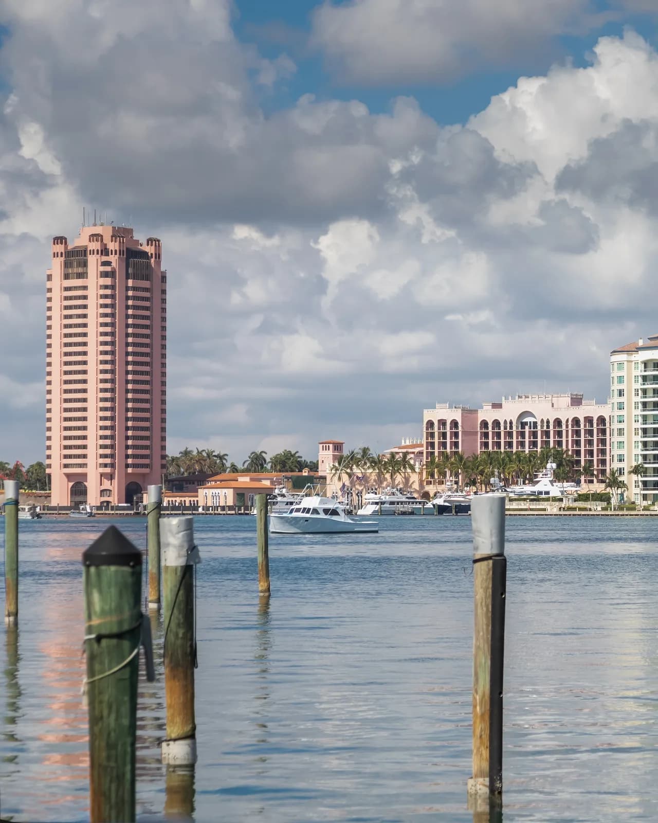 A pink high-rise tower and low waterfront buildings seen across Lake Boca Raton