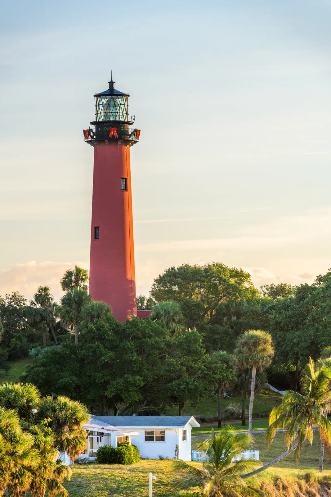 The red Jupiter Inlet lighthouse rising above palms and live oaks at golden hour