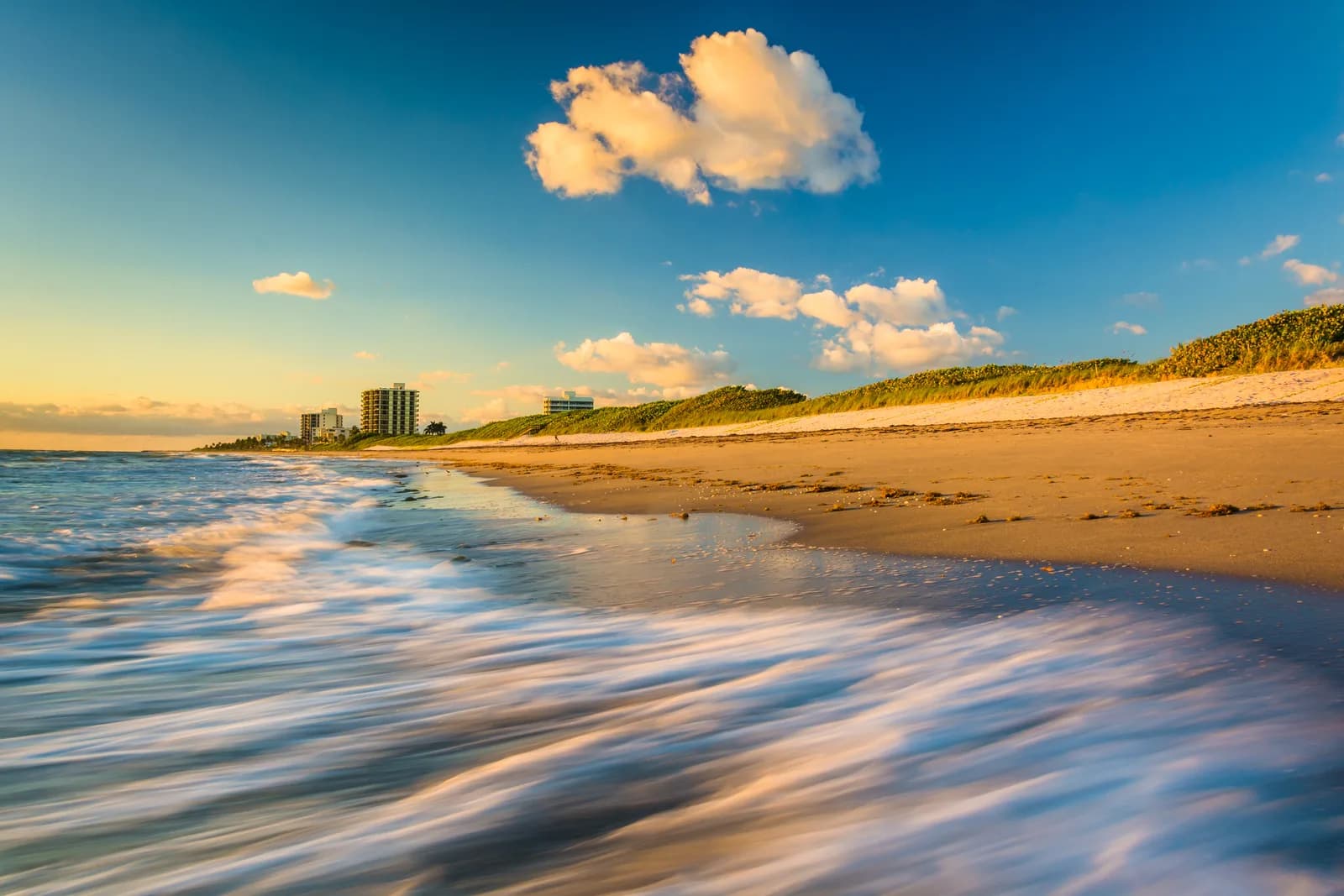 Surf washing across a wide beach at sunrise below low dunes