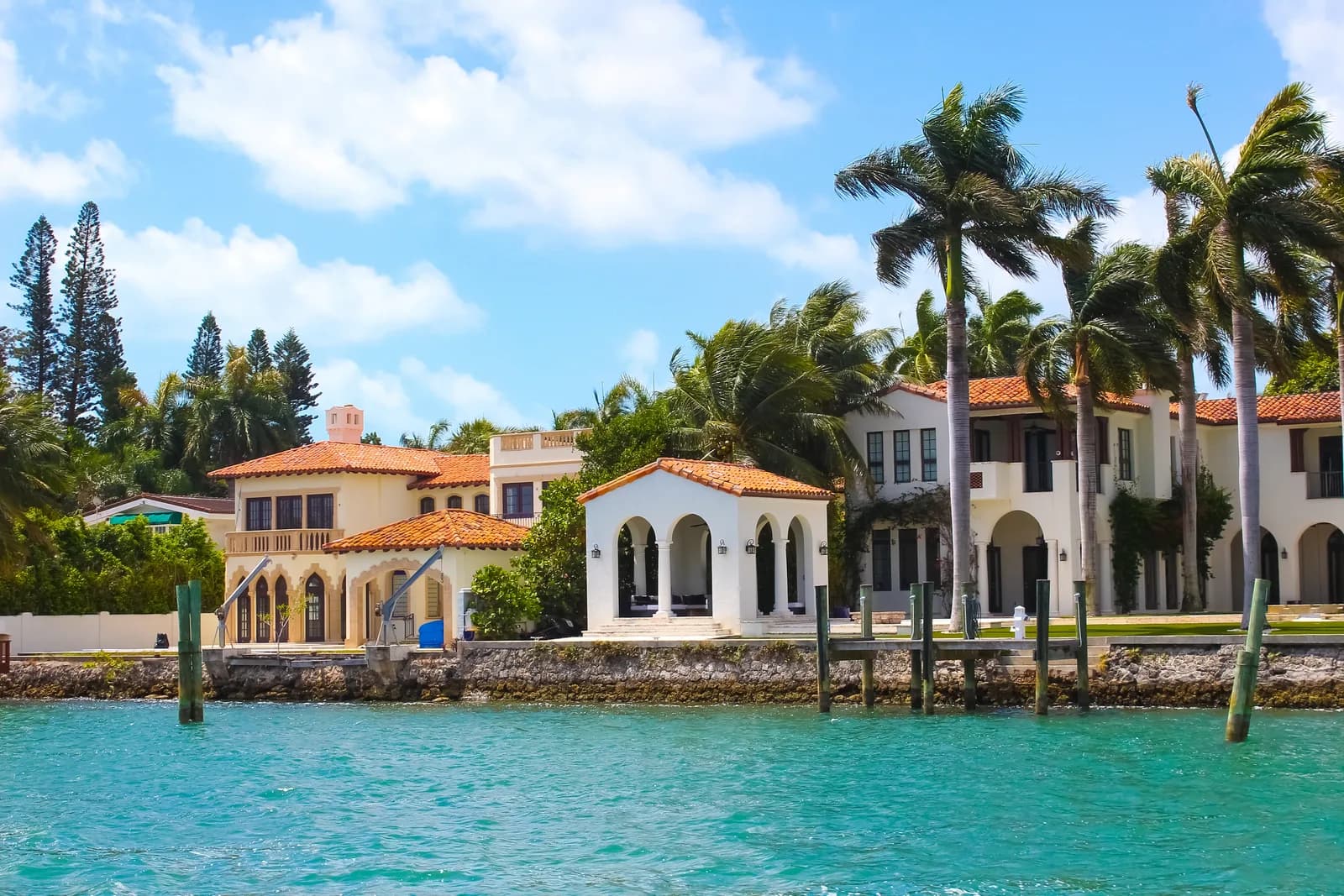 Waterfront villas with red tile roofs and arched loggias behind tall palms