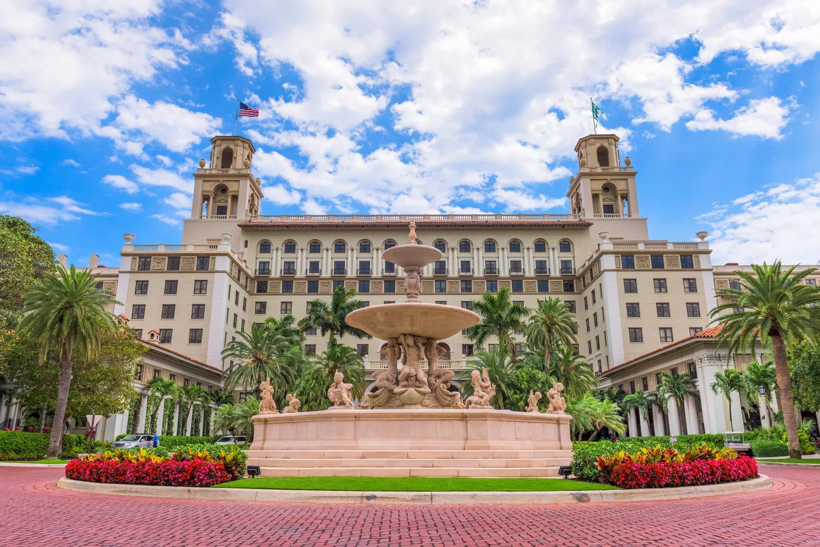 A twin-towered Mediterranean Revival resort facade behind a tiered stone fountain and flower beds