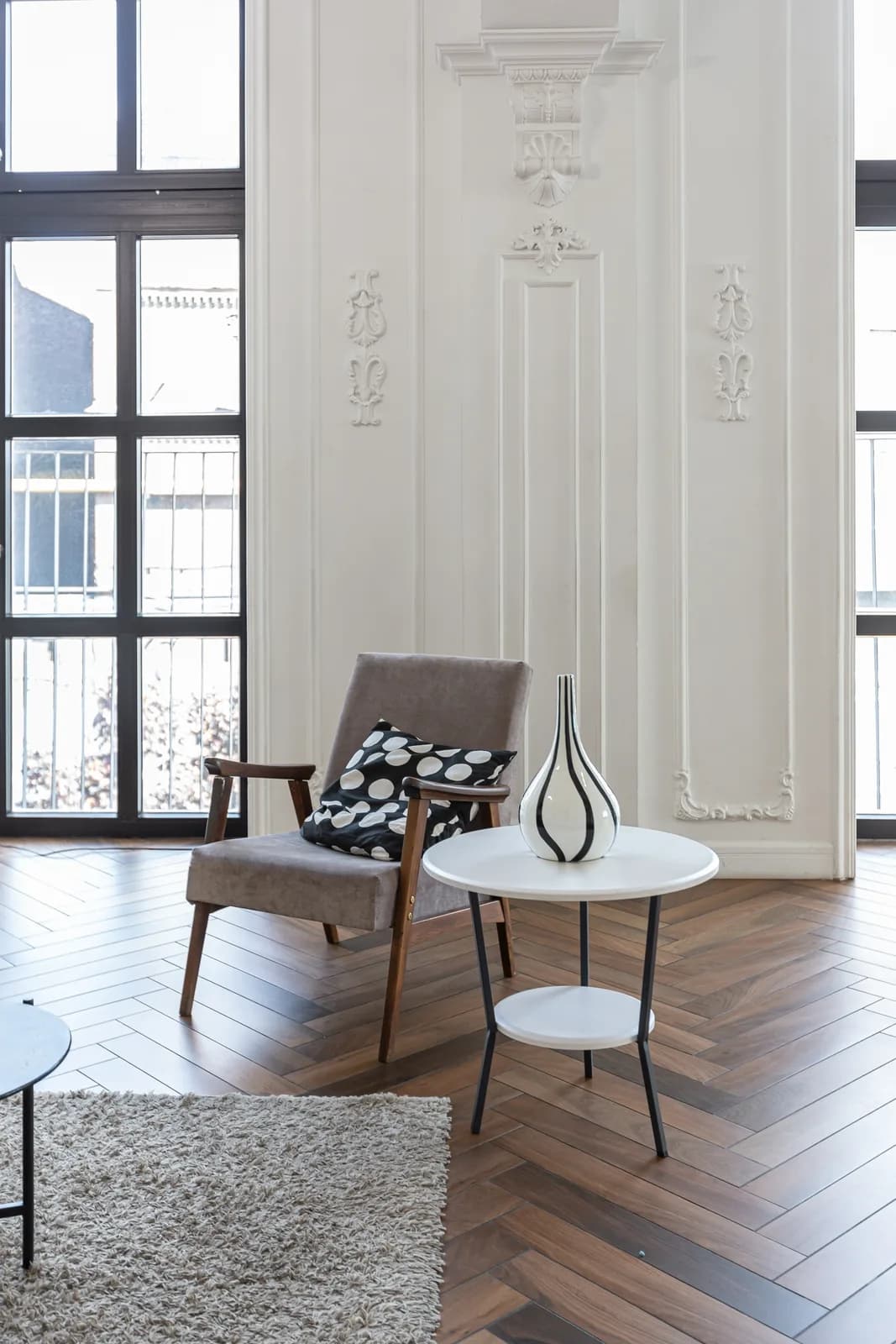 An armchair and small round table in a tall panelled room with herringbone parquet and ornamental plasterwork