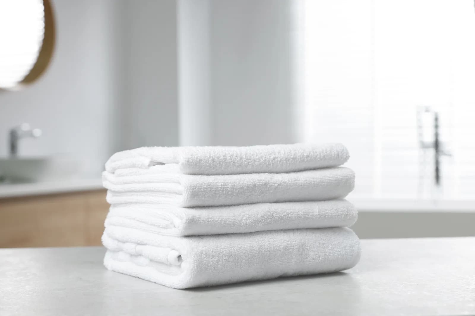 Folded white bath towels stacked on a stone counter in a bright bathroom