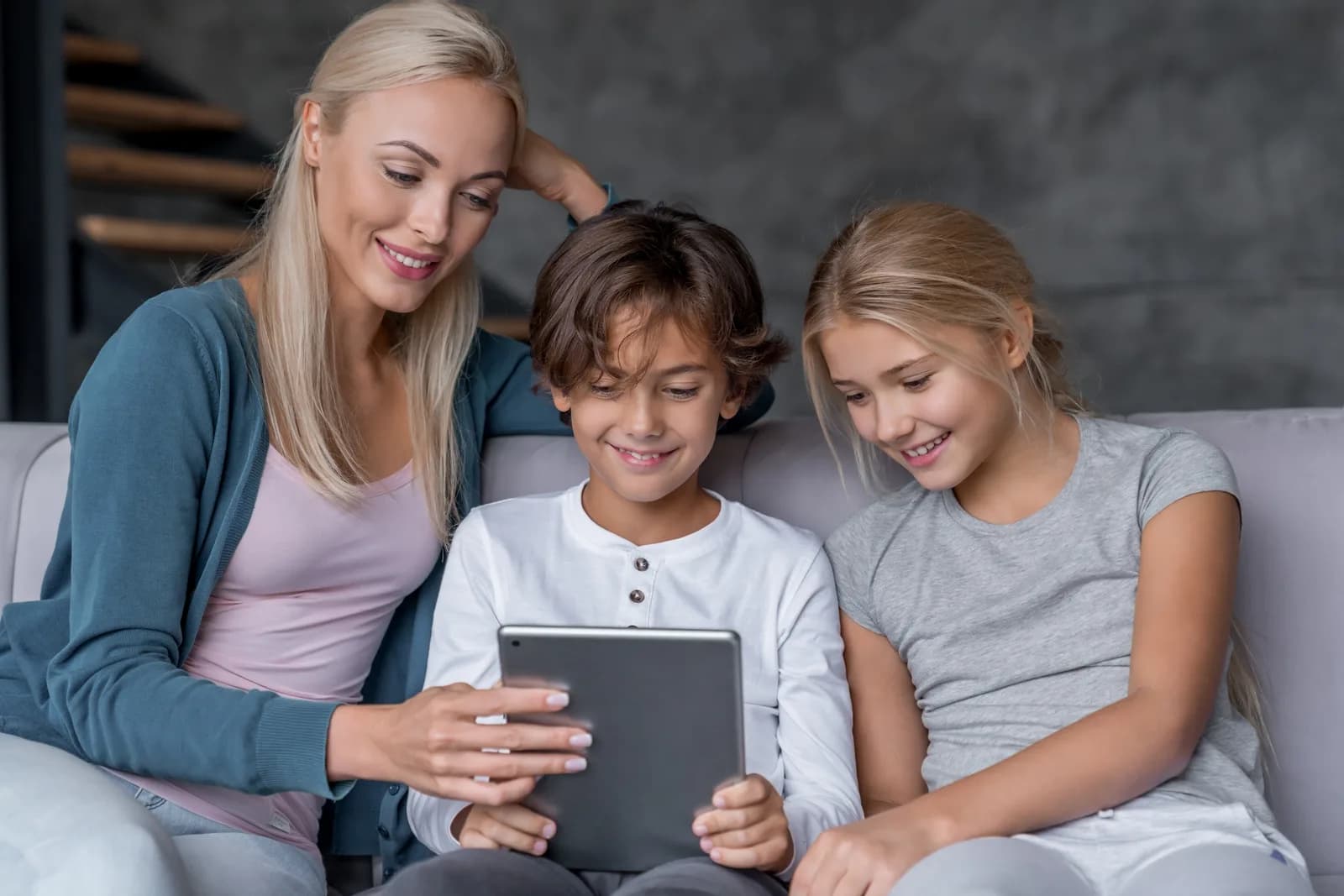 A woman, a boy and a girl looking at a tablet together on a sofa