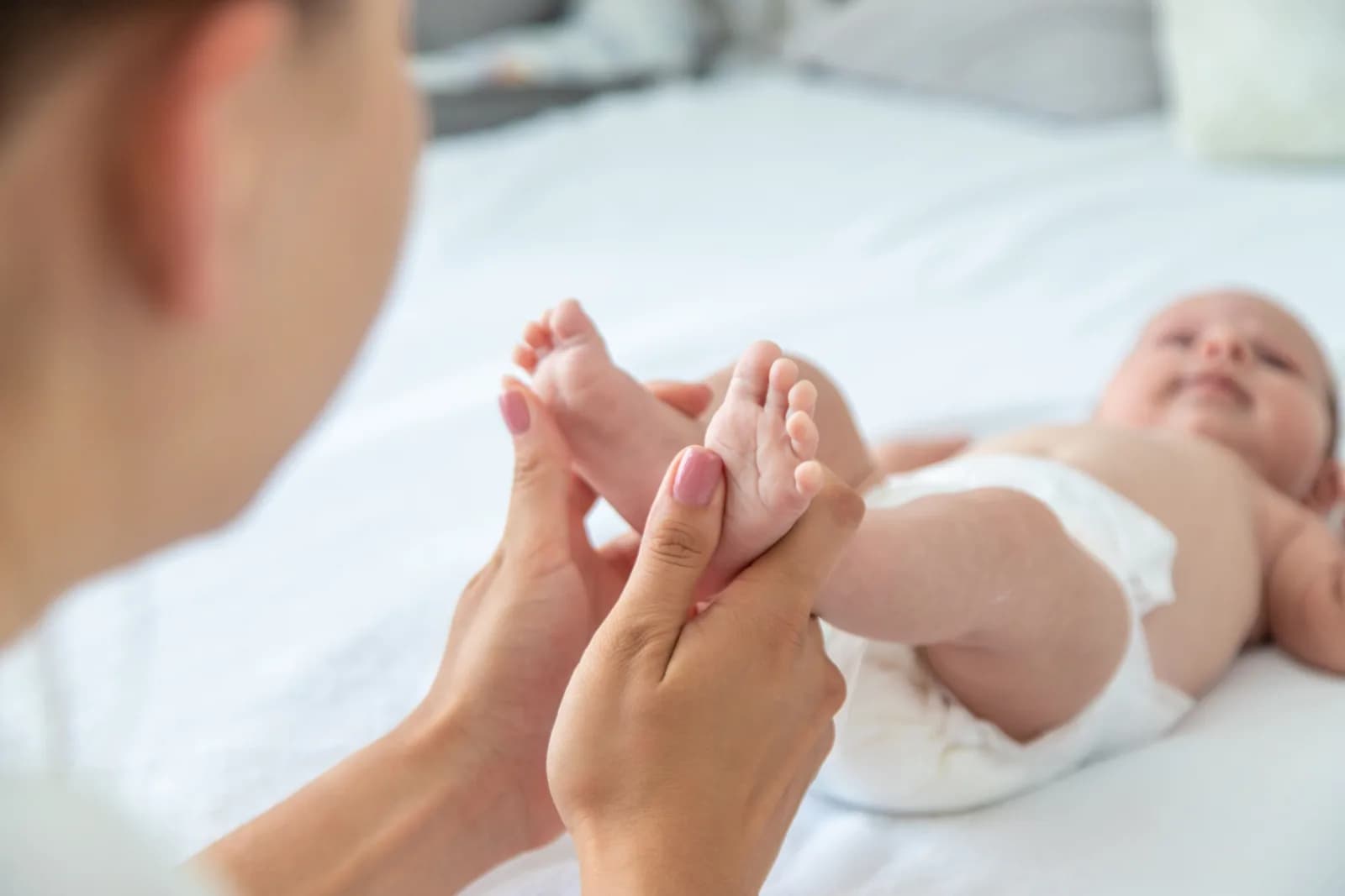 Adult hands cradling a newborn's feet on a white bed